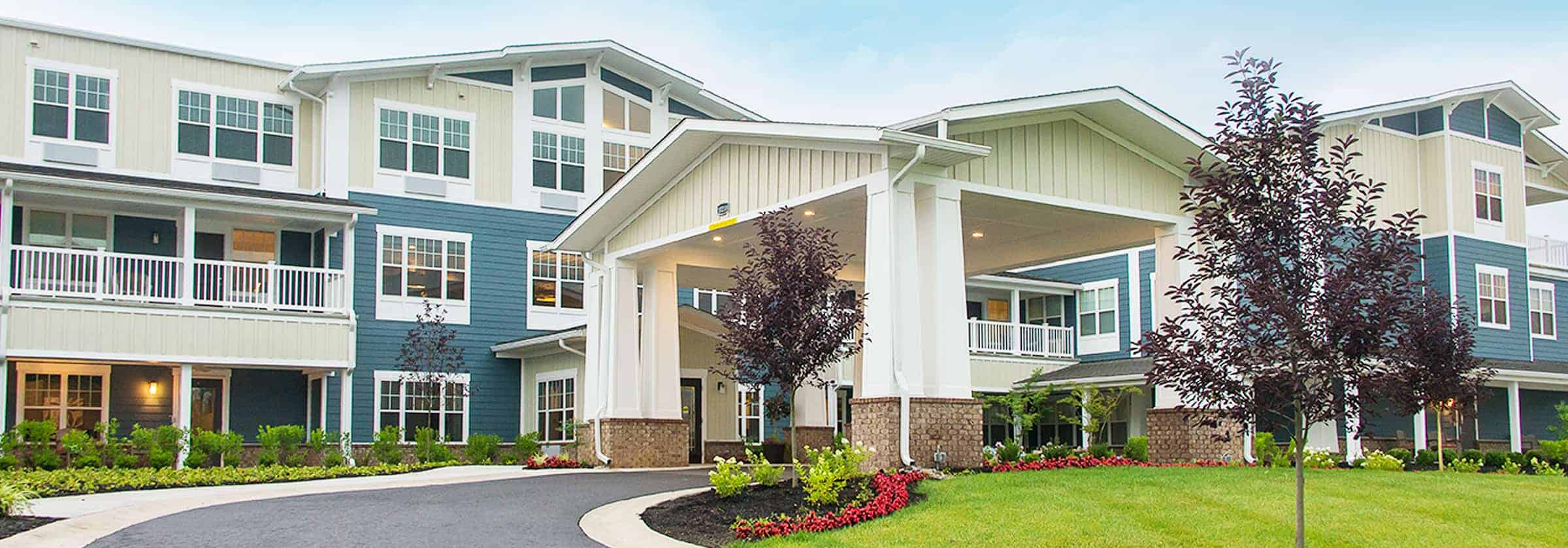 View of the front f a blue and white Traditions Management senior living community building