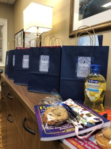 A close up with multiple navy gift bags, puzzles, masks, a bag of cookies tied with a blue ribbon, Softsoap Soap, and two pens