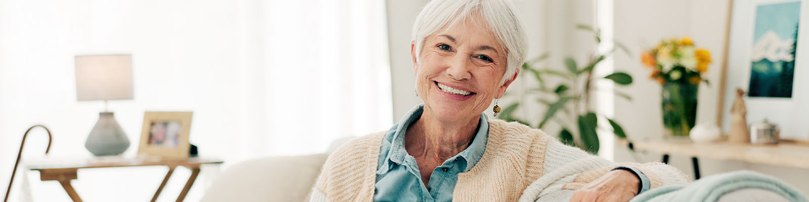 A senior woman sitting on the couch while smiling in her independent living apartment