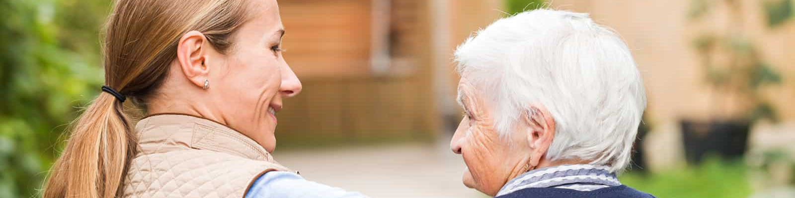 A senior woman with Alzheimer's disease looking up at her nursing assistant as they walk outside