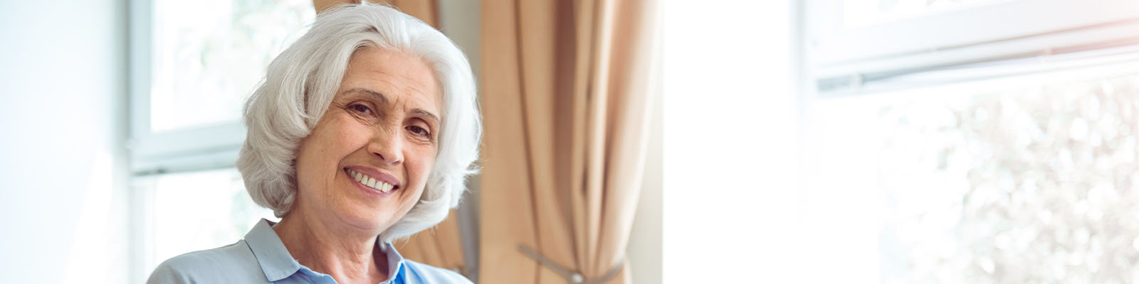 A senior woman with white hair sitting in a wheelchair and holding a laptop while smiling