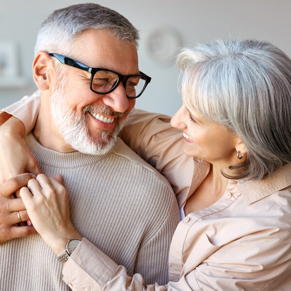 A senior man and woman sitting together on a park bench smiling and laughing together