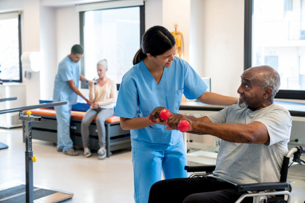 Female caregiver helping a male senior assisted living resident complete a workout in the Traditions at Camargo gym