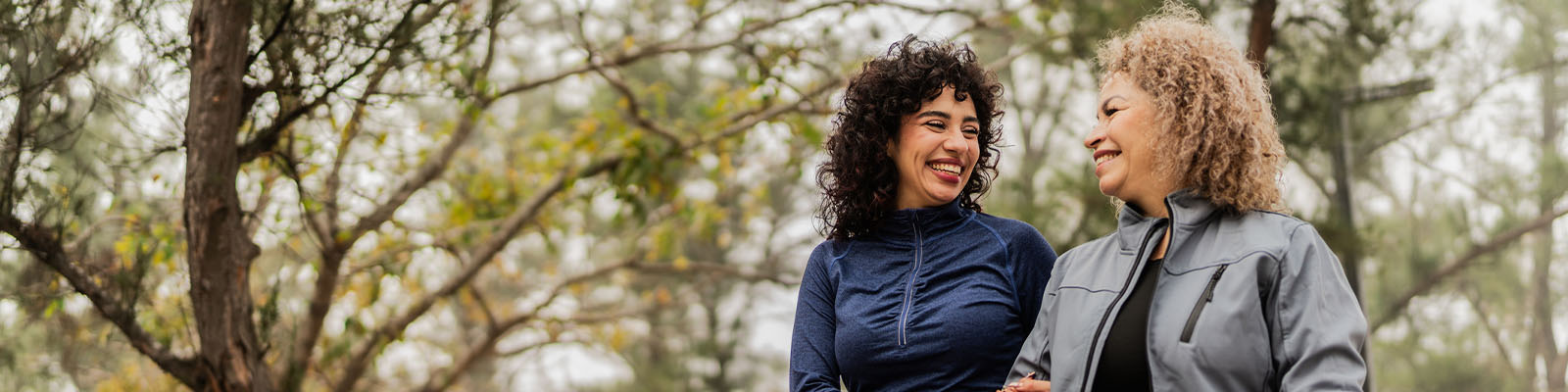 A mature woman walking with her daughter outdoors in a park as they smile at each other