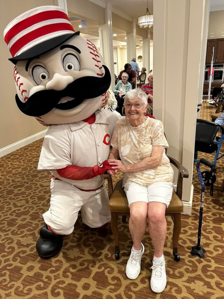 Resident poses with the Cincinnati Reds mascot, Mr. Redlegs, during a special Reds-themed community event at Traditions at Camargo.