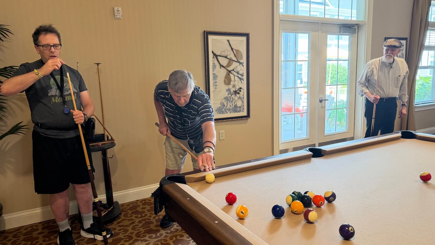 three elderly men playing pool around a billiards table in the Club Room at Traditions at Camargo in Madeira Ohio